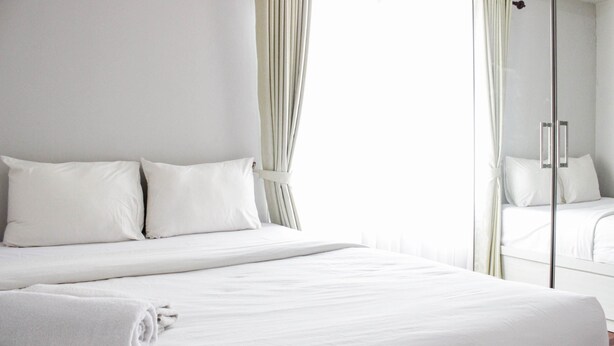 Une chambre d’hôtel avec un grand lit, deux oreillers, une serviette roulée et une porte vitrée donnant sur la salle de bain.