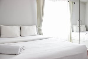 Une chambre d’hôtel avec un grand lit, deux oreillers, une serviette roulée et une porte vitrée donnant sur la salle de bain.