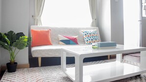Un salon moderne avec un canapé blanc, des coussins colorés, une table basse blanche et une plante en pot.