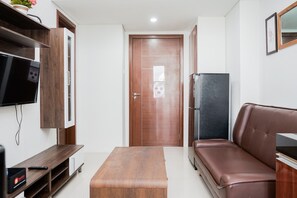 A compact living space with a wooden entertainment unit, a flat-screen TV, a brown leather sofa, a wooden coffee table, and a refrigerator. - Comfort 2BR Apartment at Vittoria Residence (Jakarta)