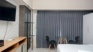 Une chambre d’hôtel moderne équipée d’un lit, d’un bureau avec un téléviseur à écran plat, d’une petite table avec des chaises et d’une grande fenêtre avec des rideaux.