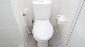 A white toilet with a flush handle, a flush button, and a toilet paper holder. - Cozy Room 2BR at 19 Avenue Apartment (Tangerang)