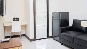 A room with a desk, a chair, a black leather sofa, a television, and a refrigerator. - Cozy Room 2BR at 19 Avenue Apartment (Tangerang)
