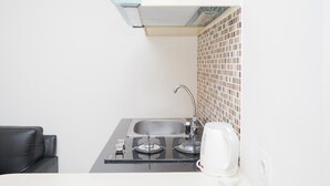 A compact kitchen with a sink, two burners, and a coffee maker. - Cozy Room 2BR at 19 Avenue Apartment (Tangerang)