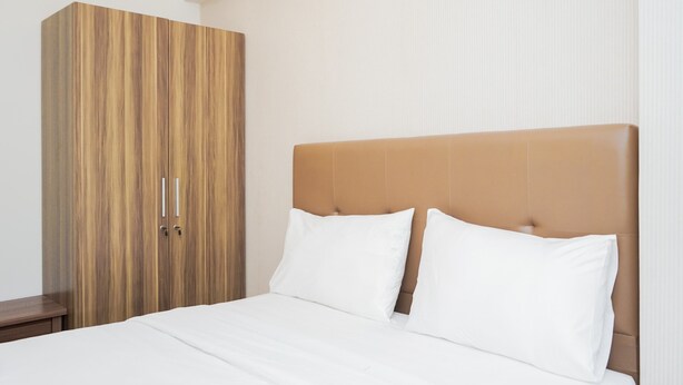 A bedroom with a bed, a wooden wardrobe, and a headboard. - Cozy Room 2BR at 19 Avenue Apartment (Tangerang)