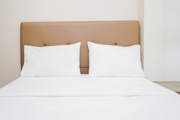 A bed with a headboard, white bedding, and a plain wall in the background.