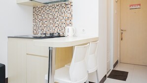 A compact kitchen with a tiled backsplash, a kettle, and white chairs. - Cozy Room 2BR at 19 Avenue Apartment (Tangerang)