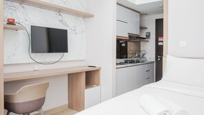 Ein modernes Hotelzimmer mit einem Bett, einem Schreibtisch mit Fernseher, einem Sessel und einer Küchenzeile.