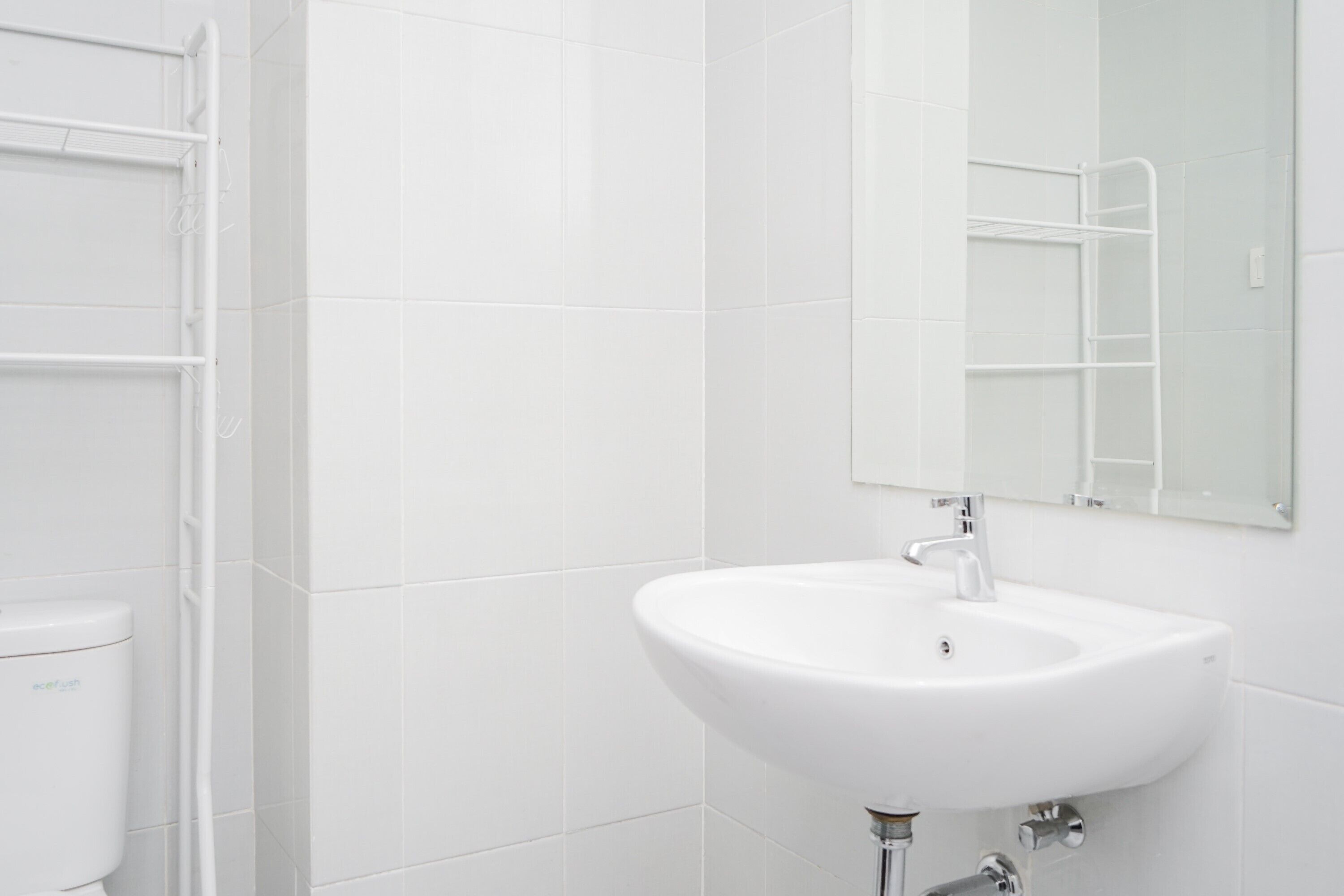 A bathroom with white tiles, a white sink, and a white toilet.