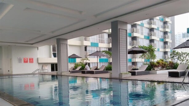 A swimming pool with lounge chairs and umbrellas, surrounded by a multi-story building with balconies. - Fully Furnished with Comfortable Design Studio Apartment H Residence (Jakarta)