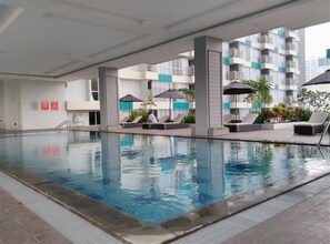 A swimming pool with lounge chairs and umbrellas, surrounded by a multi-story building with balconies. - Fully Furnished with Comfortable Design Studio Apartment H Residence (Jakarta)