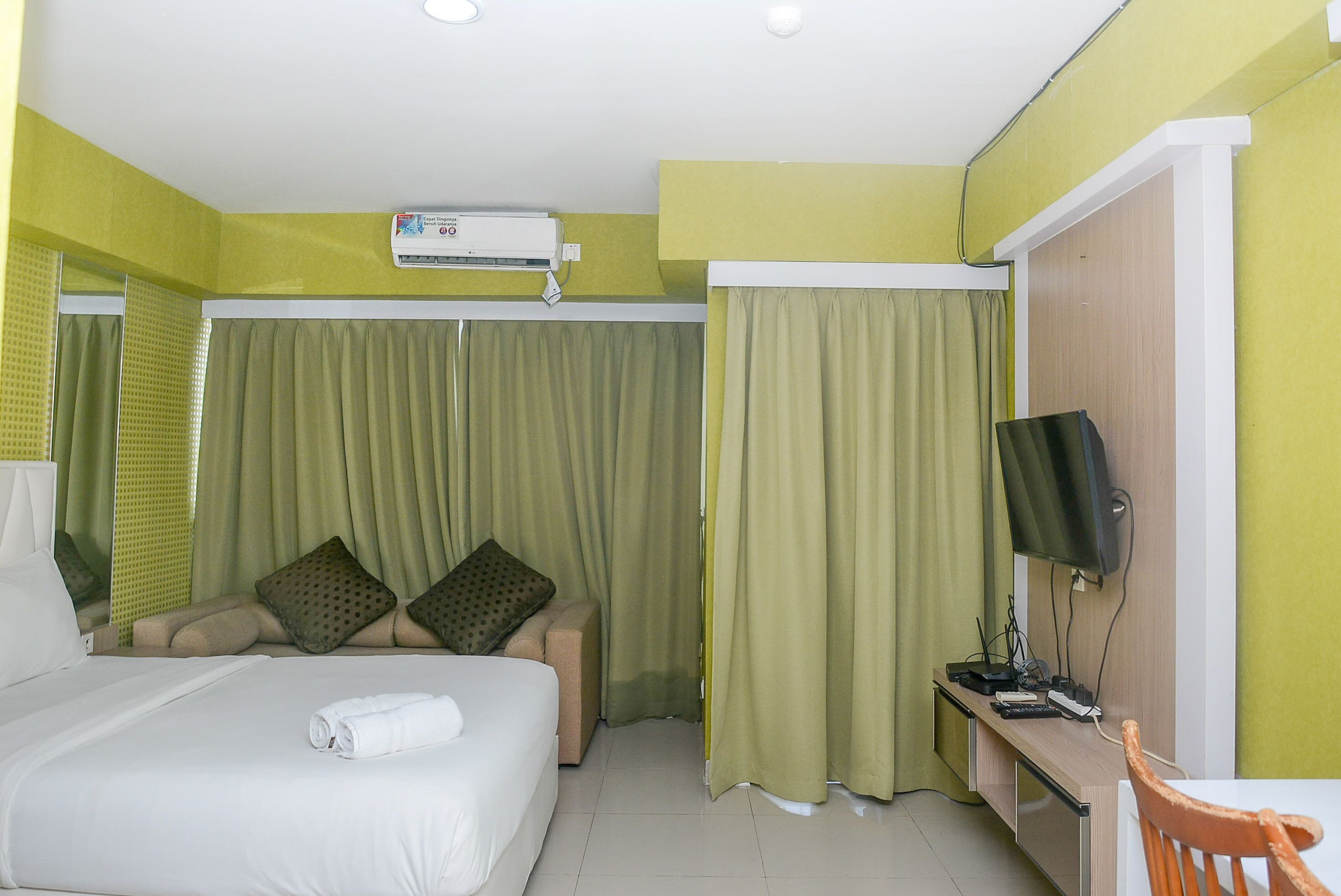 A hotel room with a bed, a desk with a computer and a TV, and a window with curtains.