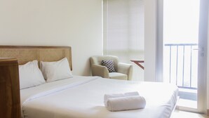 A hotel room with a large bed, a chair, a window with blinds, and a balcony.