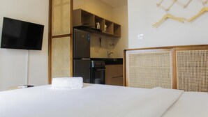 A hotel room with a bed, a television, a kitchenette, and a wall-mounted clothes rack.