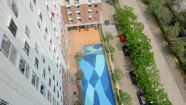 A high-rise building with multiple balconies, a rooftop pool with a geometric pattern, and a parking area adjacent to a tree-lined street. - Alluring Studio at Lagoon Apartment near Bekasi Town Square (Bekasi)
