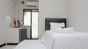 A hotel room with a bed, a small table, a window with a view, and a wall-mounted air conditioner. - Alluring Studio at Lagoon Apartment near Bekasi Town Square (Bekasi)