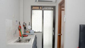 A small kitchen with a sink, faucet, and dish rack. There is a window with a frosted glass door and a door with a handle. - Alluring Studio at Lagoon Apartment near Bekasi Town Square (Bekasi)