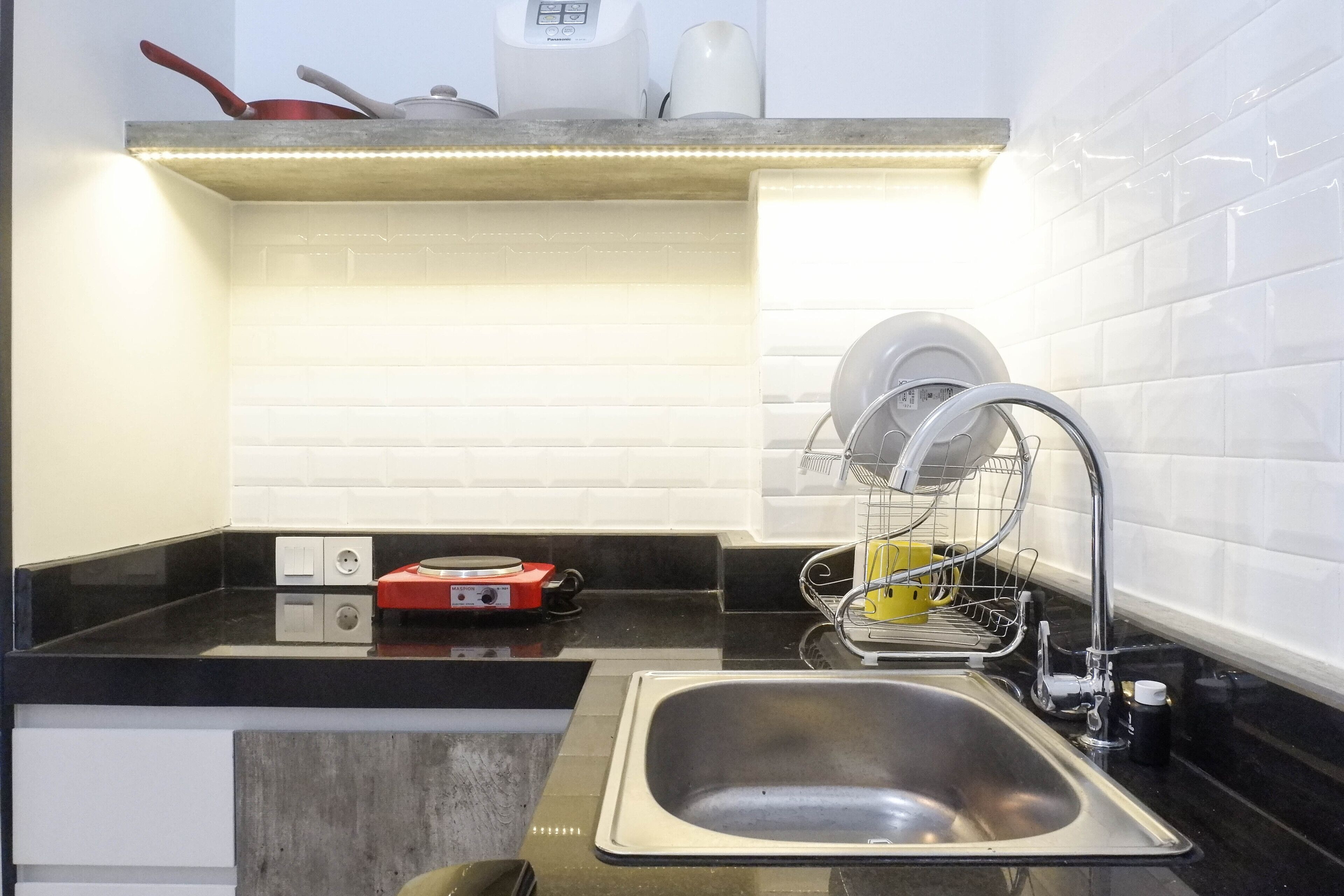 Cozinha com pia de aço inoxidável, escorredor de louça, fogão elétrico vermelho e painel de azulejos branco.