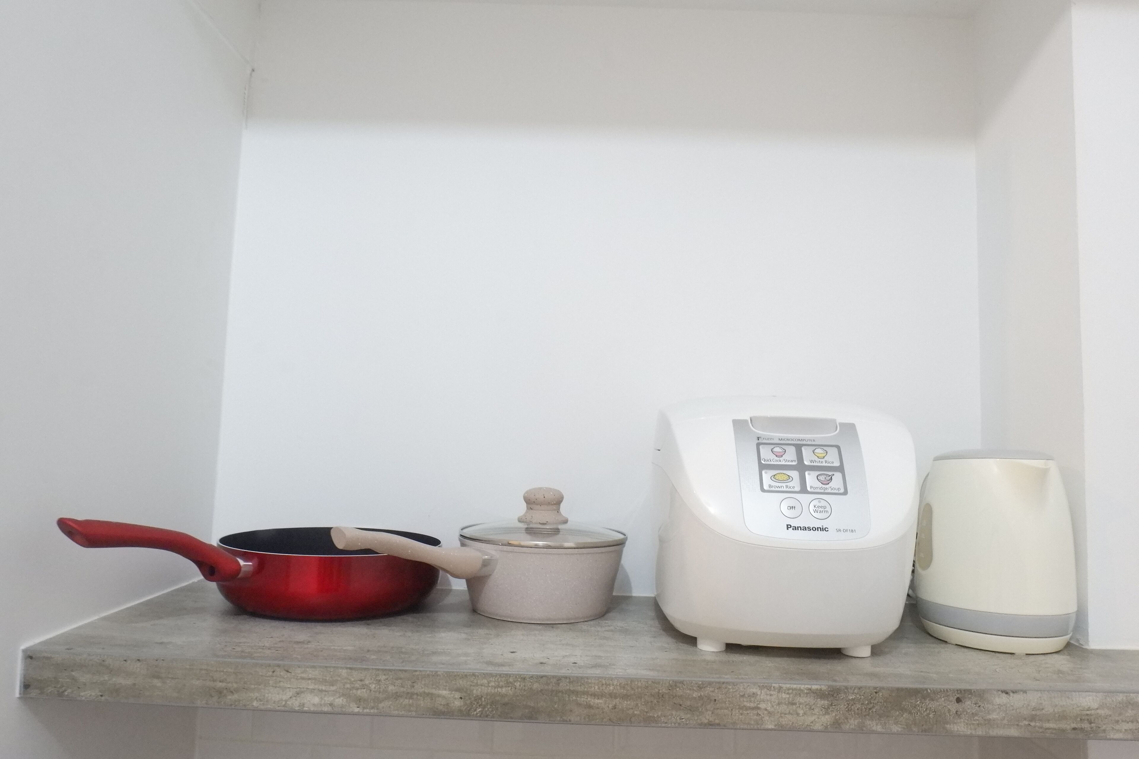 A kitchen counter with a red pan, a white rice cooker, and a white appliance with a control panel.