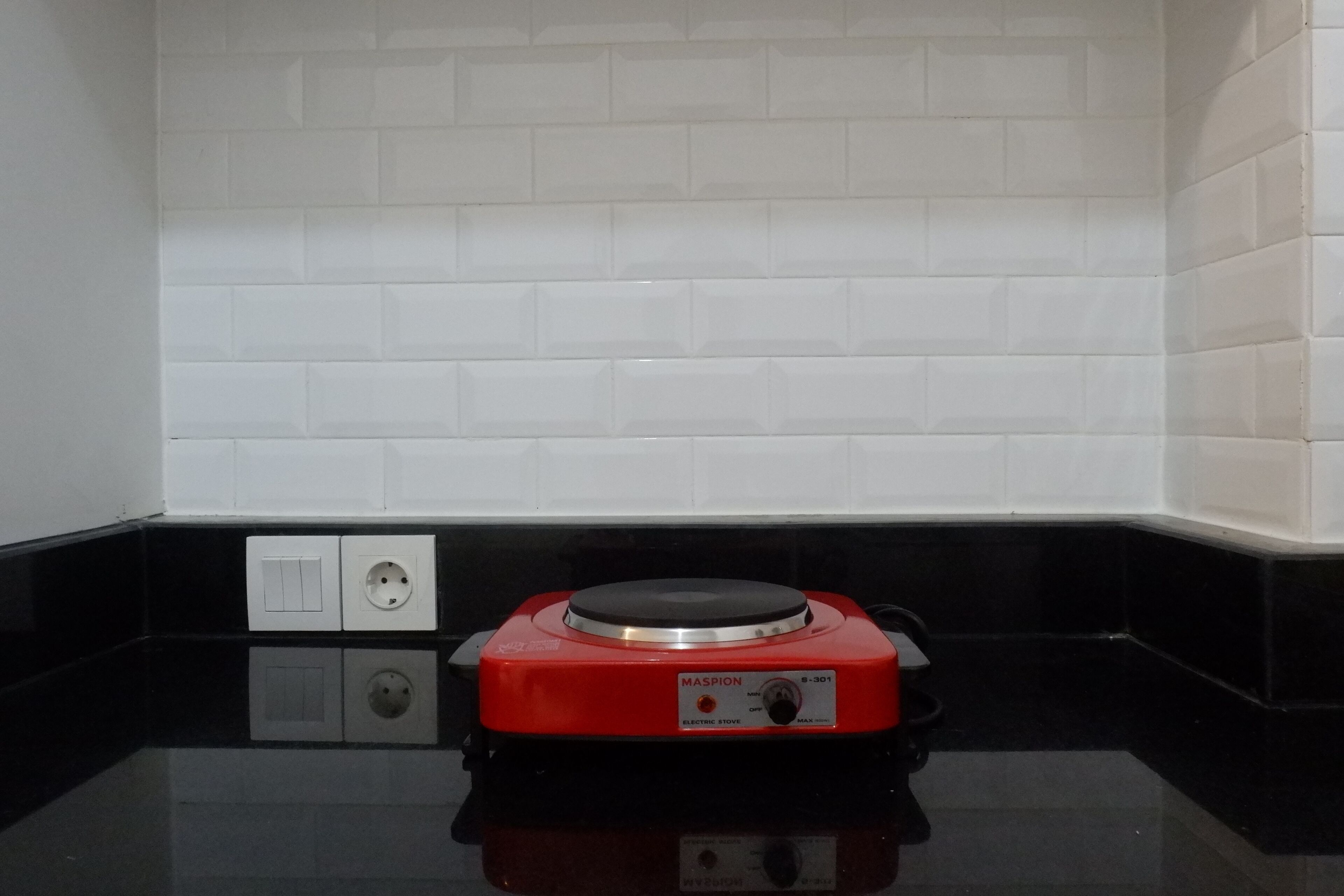 A red electric stove with a control panel, two electrical outlets, and a black countertop.