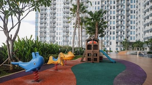 A children's play area with colorful equipment, a slide, and a small treehouse structure. - Modern Luxurious Studio Room at Anderson Supermall Mansion Apartment (Surabaya)