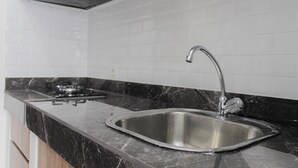 A kitchen with a stainless steel sink, a gas stove, and white subway tiles on the wall. - Strategic and Comfy Studio Casa De Parco Apartment (Pagedangan)