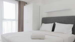 A neatly made bed with white linens and a rolled towel, a grey headboard, and a white wardrobe. - Strategic and Comfy Studio Casa De Parco Apartment (Pagedangan)