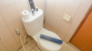 A standard bathroom with a toilet, a roll of toilet paper, and a blue towel on the seat.