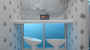A room with two white pedestal sinks, a window with a view, and a travelio sign on the wall.