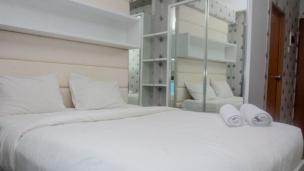 A neatly made bed with white linens and two rolled towels, a glass-fronted wardrobe, and a wooden door.