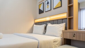 A neatly arranged hotel room with a bed, a bedside table, and a small seating area.