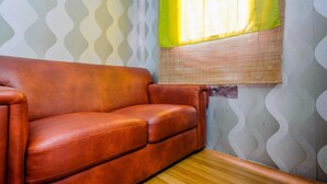 Une pièce avec un canapé en cuir marron, une fenêtre avec des rideaux jaunes et un papier peint à motifs.