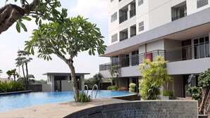 A modern building with a swimming pool, surrounded by greenery and a clear sky.