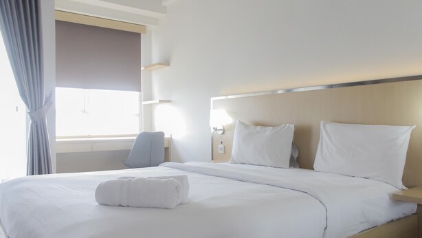 A hotel room with a large bed, a bedside table, a chair, and a window with curtains.