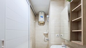 A bathroom with a white sink, a mirror, a handheld showerhead, and a wall-mounted heater. - Bright Studio Apartment at Springwood Residence (Tangerang)