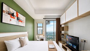 A hotel room with a bed, a desk, a television, and a view of the city. - Bright Studio Apartment at Springwood Residence (Tangerang)