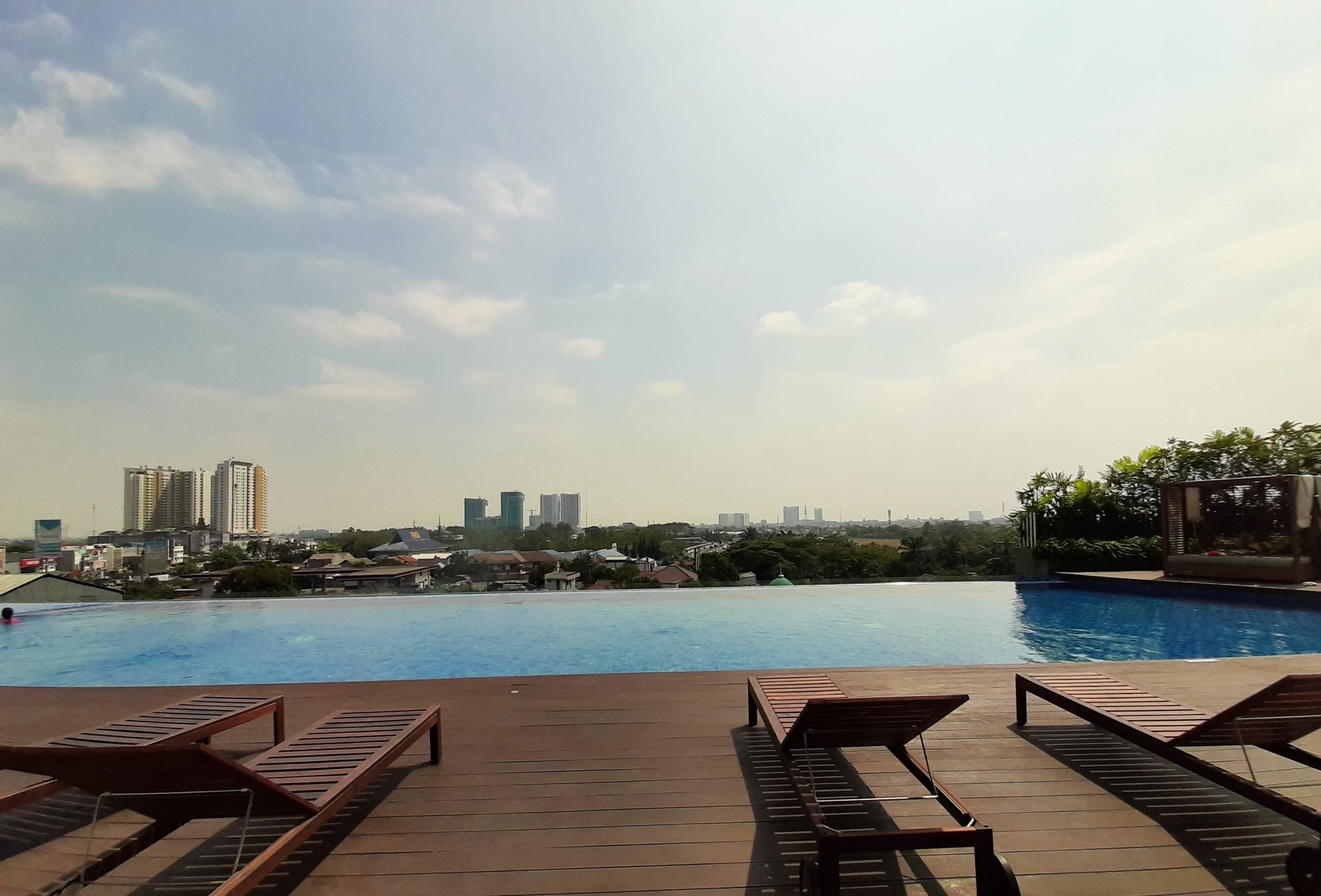 Una piscina con sillones de descanso y un paisaje urbano al fondo.