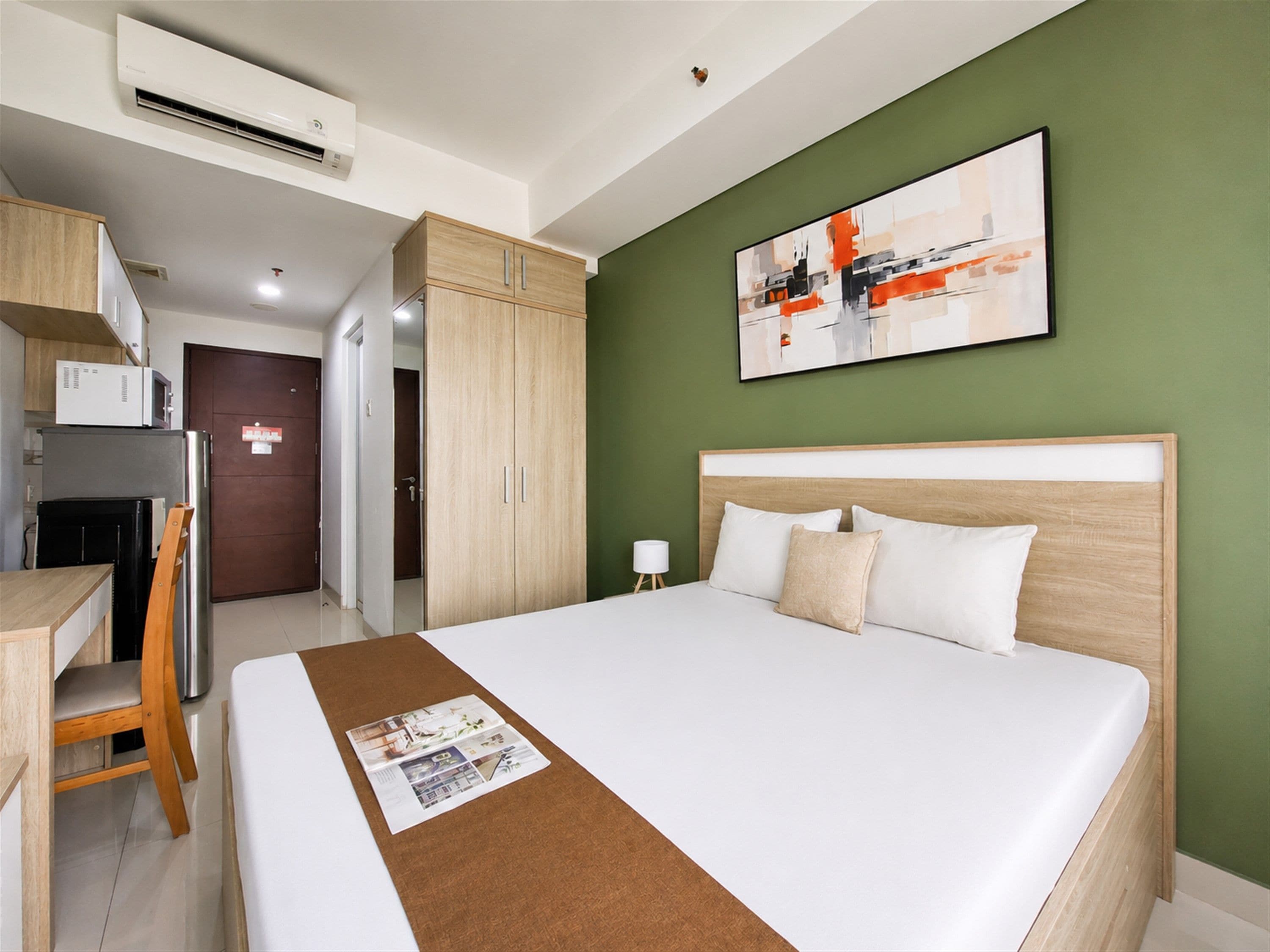 A hotel room with a bed, a desk, a chair, a microwave, and a door.