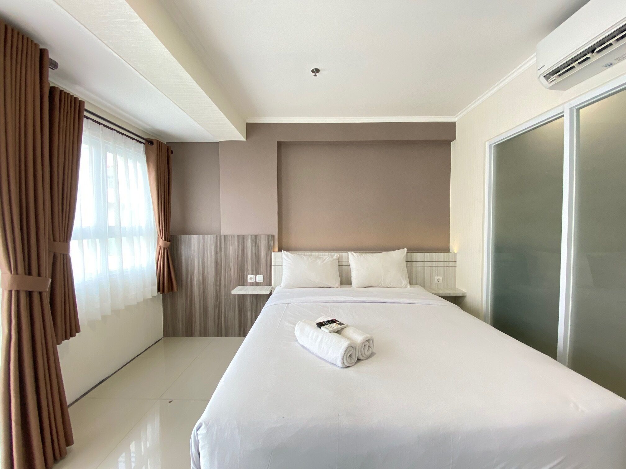 Una habitación de hotel con una cama grande, una mesita de noche, un armario y una ventana con cortinas.