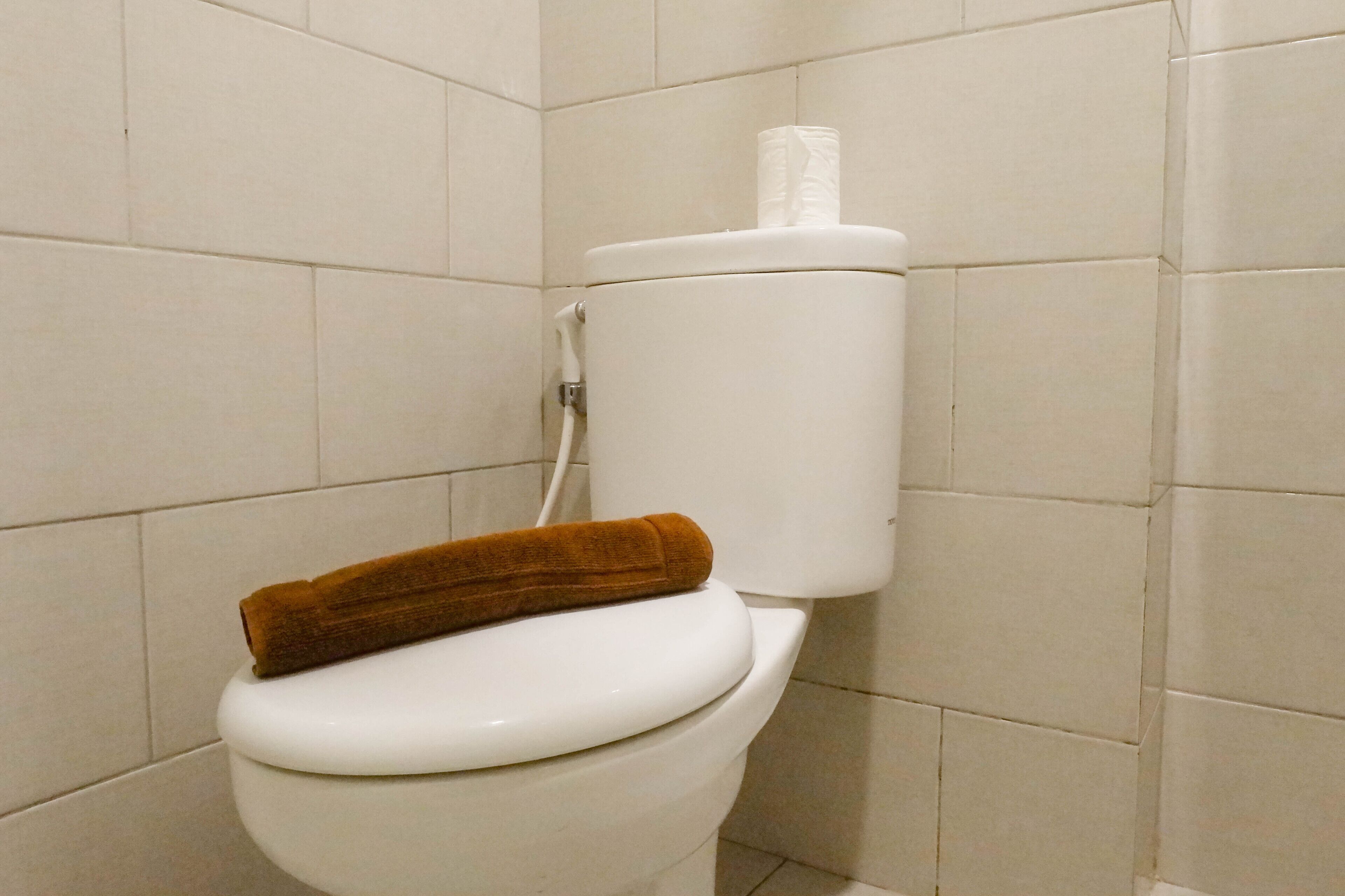 A toilet with a brown towel on the seat and a toilet paper holder on the tank.