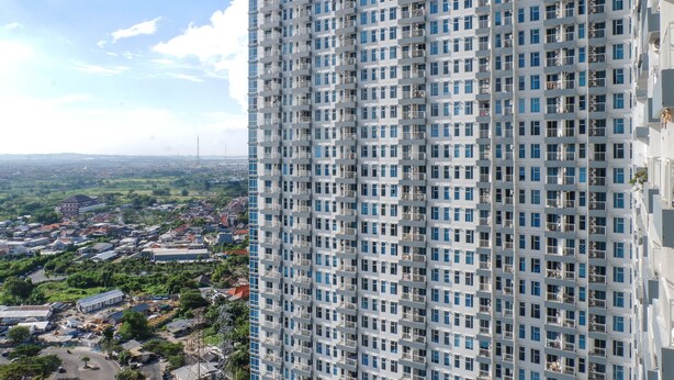 A high-rise building with a grid of windows and balconies, overlooking a cityscape with various buildings and greenery. - Best Studio Benson Apartment Connected to Pakuwon Mall next to Anderson (Surabaya)