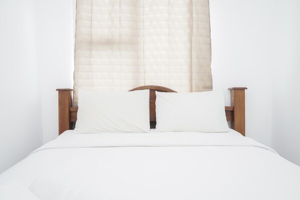 A bed with a wooden headboard, white bedding, and a sheer curtain.