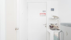 A white door with a safety sign, a small shelf with kitchen utensils, and a refrigerator. - New and Simply Studio at Urbantown Serpong Apartment (South Tangerang)