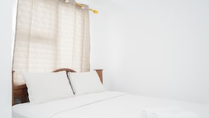 A neatly made bed with white linens and pillows, a rolled white towel, and a wooden headboard. - New and Simply Studio at Urbantown Serpong Apartment (South Tangerang)