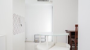 A minimalist room with a round glass table, white chairs, a wooden chair, and a patterned wall. - New and Simply Studio at Urbantown Serpong Apartment (South Tangerang)