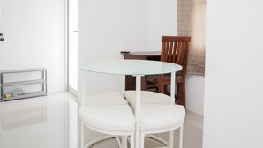 A small, modern dining area with a glass-top table, white chairs, and a wooden chair. - New and Simply Studio at Urbantown Serpong Apartment (South Tangerang)