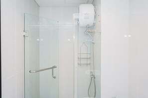 Ein Duschraum mit Glaswänden, einer Handbrause, einem Handtuchhalter und einem Toilettenpapierhalter.