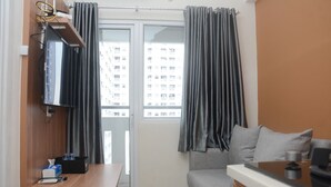 A compact living space with a sofa, a small table, a TV mounted on the wall, and a window with curtains.