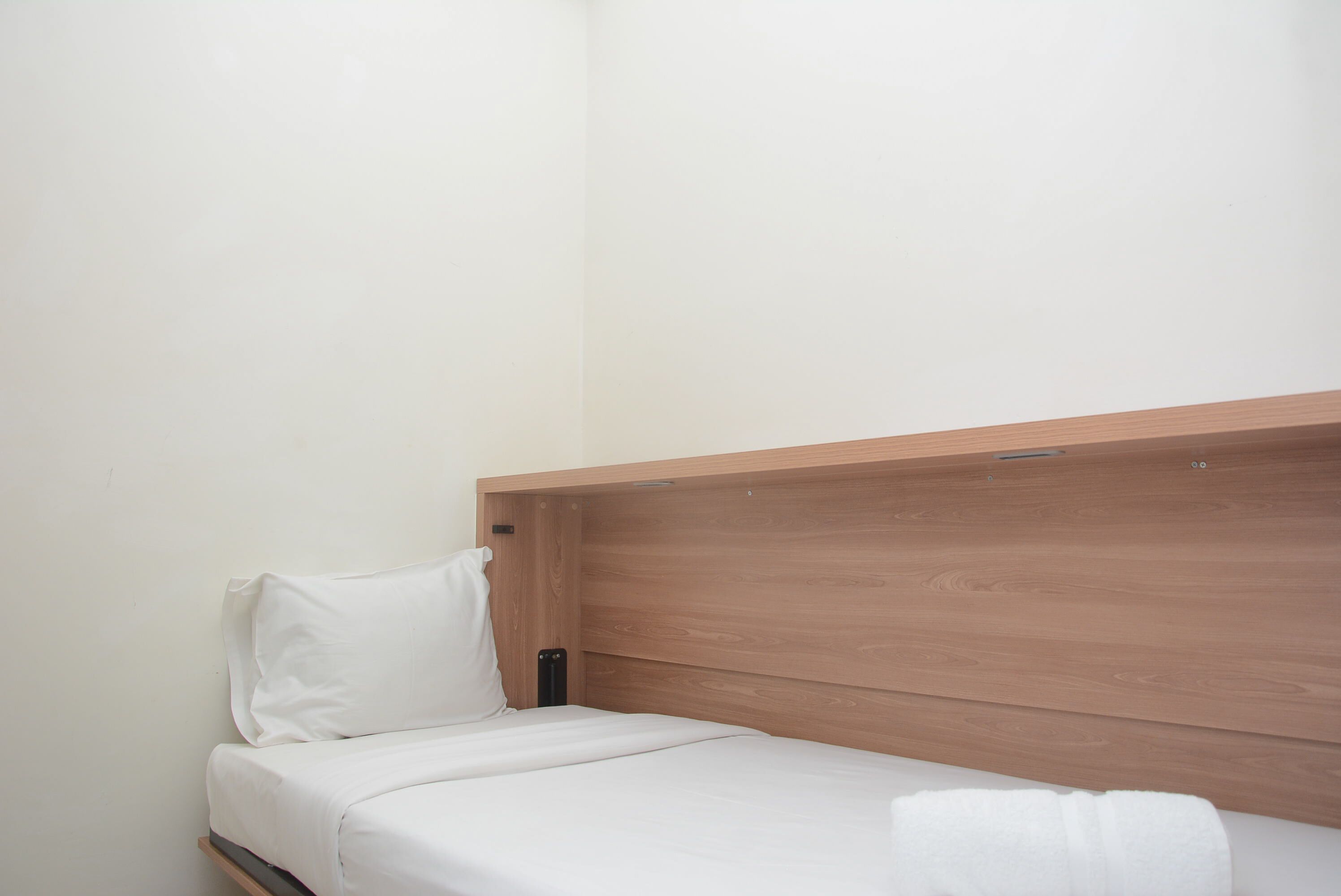 A small, single-bed room with a wooden headboard and white bedding.