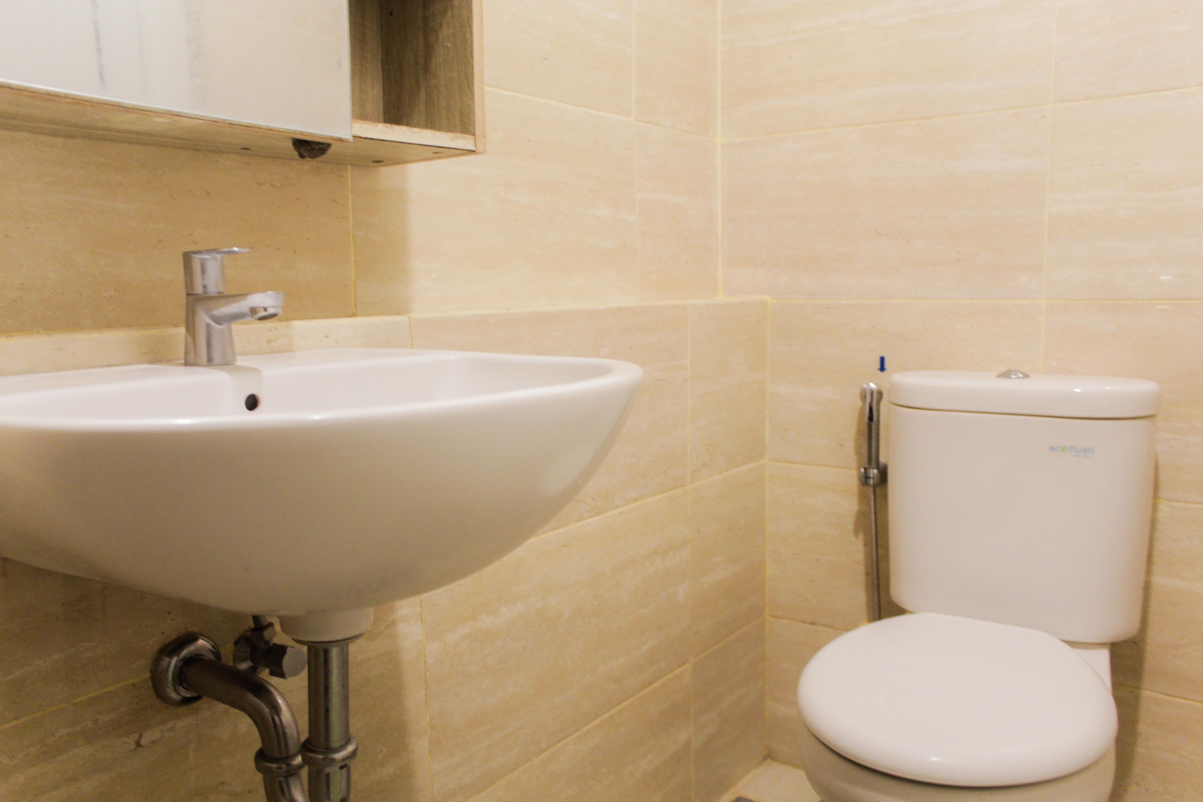 A bathroom with a white sink and toilet, beige tiles, and a wooden cabinet above the sink.